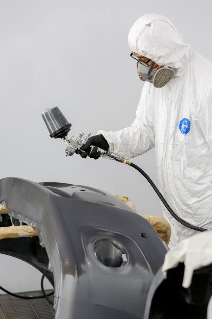 Technician in protective gear spray painting a car bumper.